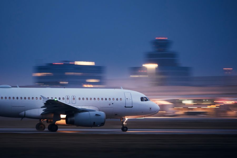 Airplane during take off on airport runway at night against air traffic control tower. Plane in blurred motion at night. 